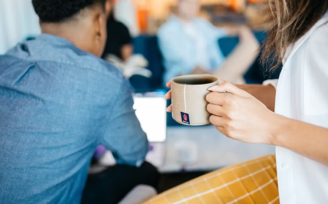 woman holding a coffee cup in front of a man looking at a tablet